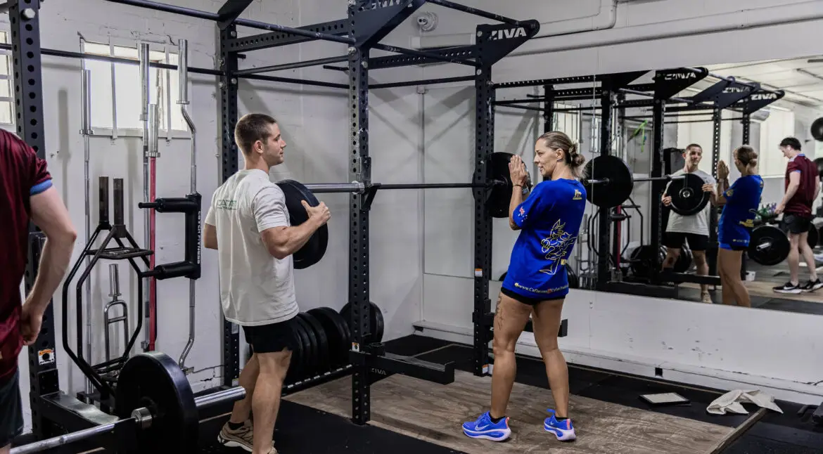 A male coach training a woman as they prepare to set up a barbell in a squat rack at CTC functional fitness gym in Randwick.