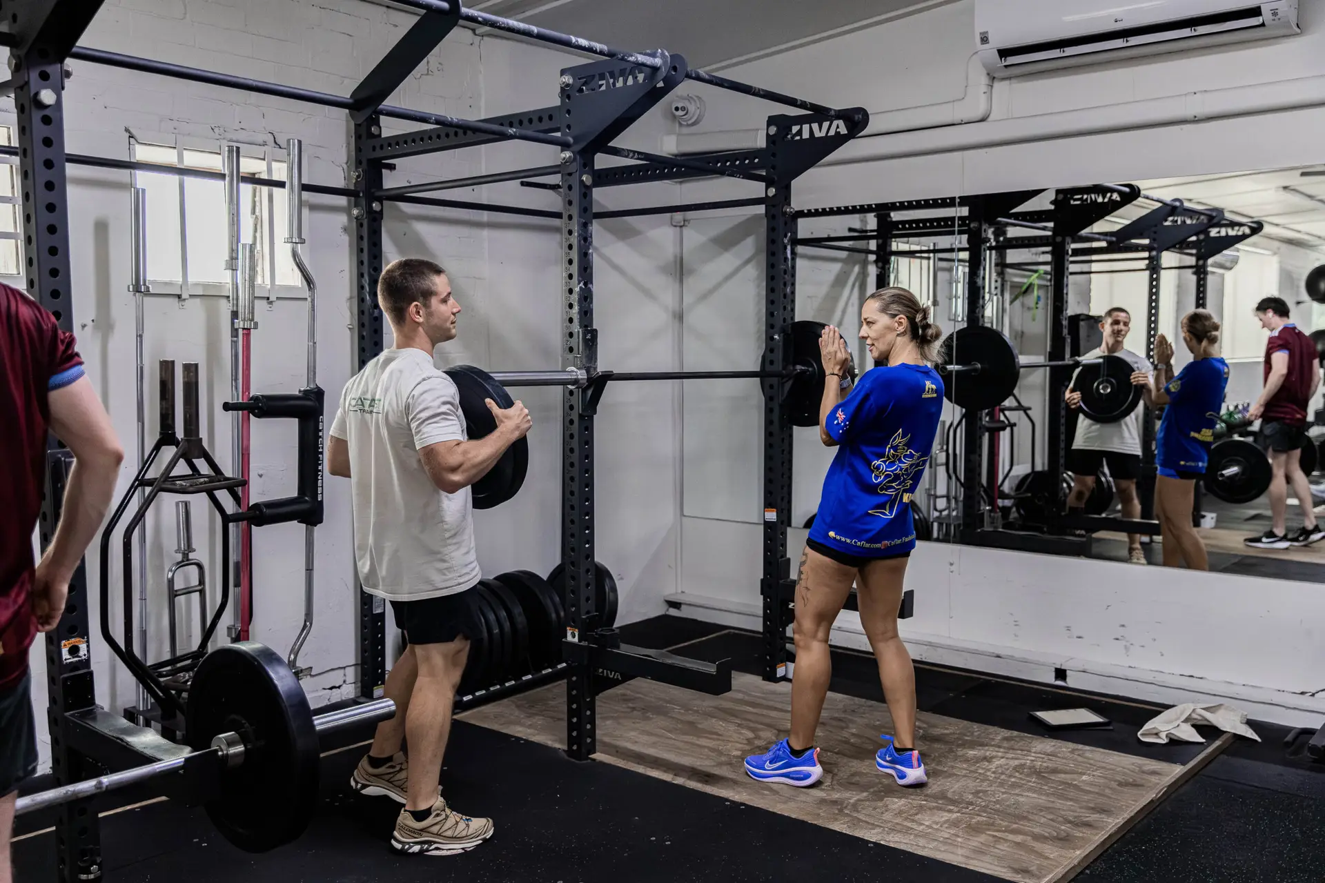 A male coach training a woman as they prepare to set up a barbell in a squat rack at CTC functional fitness gym in Randwick.