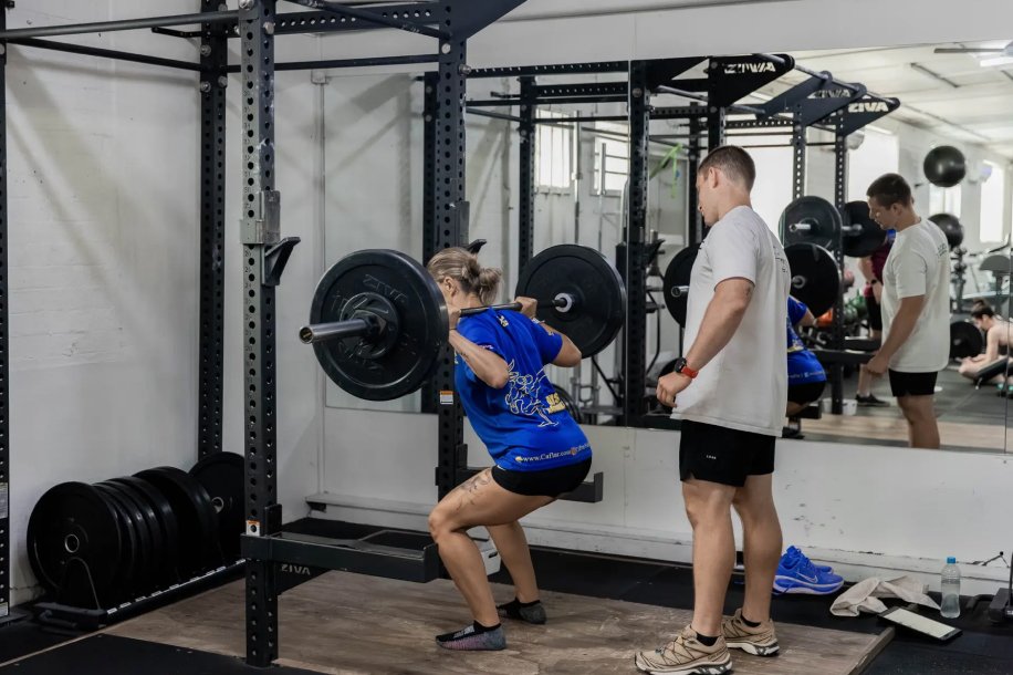 A Catalyst member back squatting with a coach spotting at Catalyst Training Co Randwick